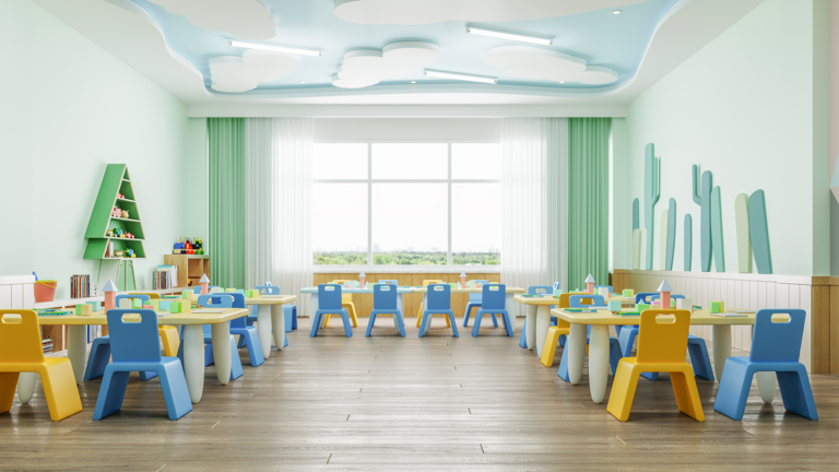 A bright, clean, and empty classroom or playroom designed for young children. The room has light green walls, a cloud-themed ceiling, and is filled with small tables and colorful yellow and blue chairs.