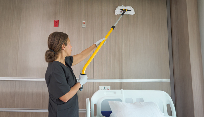 Woman cleans behind hospital bed with Rubbermaid product