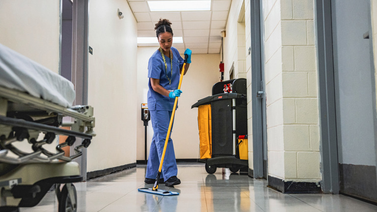 Cleaning professional mopping a hallway floor in a hospital or healthcare facility using commercial-grade equipment.